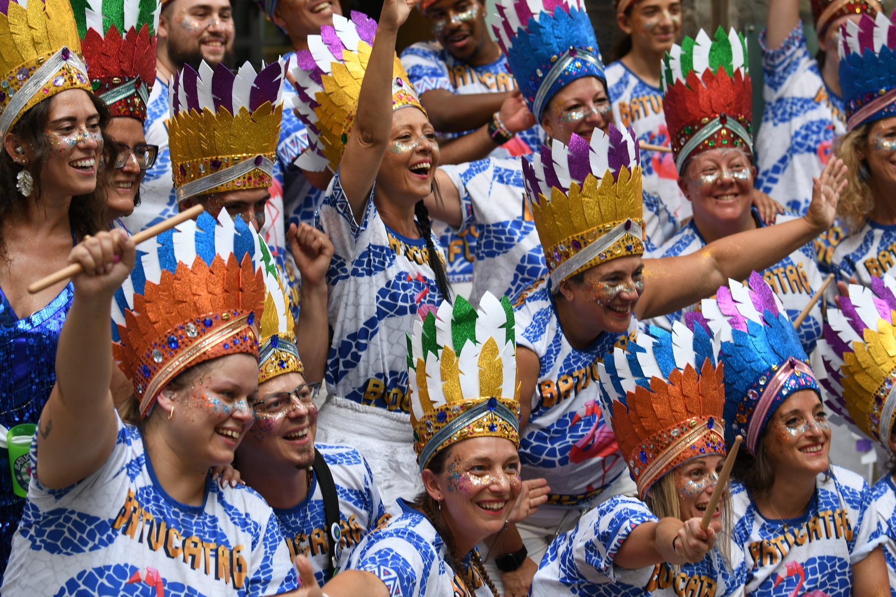 Les percussionnistes de BATUCATAG en coiffes de plumes colorées, bras levés