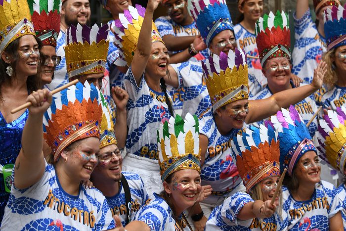 Percussionnistes de BATUCATAG en coiffes de plumes colorées, bras levés au milieu de la foule