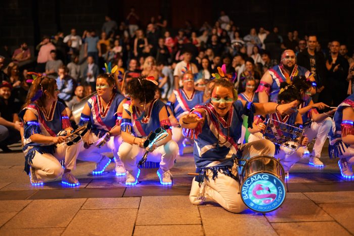 La troupe accroupie en formation devant le public, instruments illuminés, de nuit