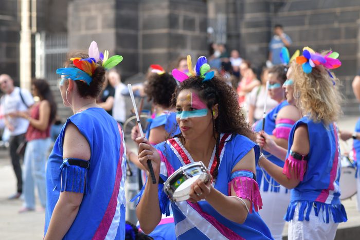Musiciennes jouant du tamborim devant une façade en pierre de Volvic
